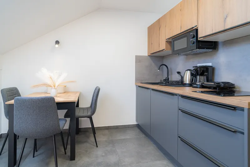 Kuhinja apartmaja 8 s sivimi omaricami in jedilno mizo s stoli